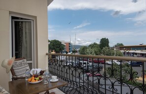 Un balcón con una mesa dispuesta para dos personas, que incluye un plato de fruta, vasos y una botella de agua.