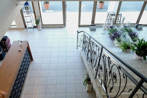 A spacious indoor area with a tiled floor, a wooden bench, a metal railing, and potted plants. - Lotus (Nessebar)