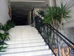 A staircase with a black wrought iron railing, potted plants, and a stone wall.