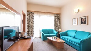 Una sala de estar moderna con un sofá color turquesa, una mesa de centro de madera, un televisor y un ventanal con cortinas estampadas.