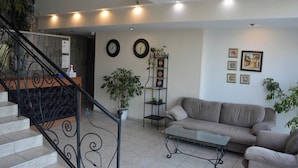 Una sala de estar con sofá, una mesa de centro, una escalera con barandilla y una pared decorada con relojes y cuadros.