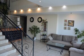 A living room with a sofa, a coffee table, a staircase with a railing, and a wall with clocks and framed pictures.