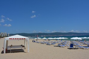 Una playa con una carpa de masajes y varias sombrillas.