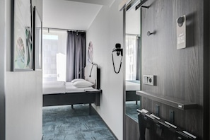 A modern hotel room with a bed, a desk, a mirror, and a window with curtains. - Hotel Fridhem (Stockholm)