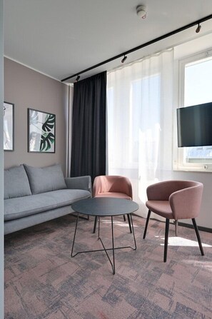 A modern living room with a grey sofa, two pink armchairs, a round coffee table, and a flat-screen TV on a wall. - Hotel Fridhem (Stockholm)