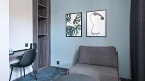 A modern room with a gray sofa, a black chair, a desk with a laptop, and two framed artworks on the wall. - Hotel Fridhem (Stockholm)