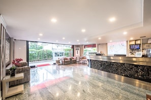 Welcome to our hotel lobby, featuring a reception desk, comfortable seating area, and a large window offering a view of the outdoors.