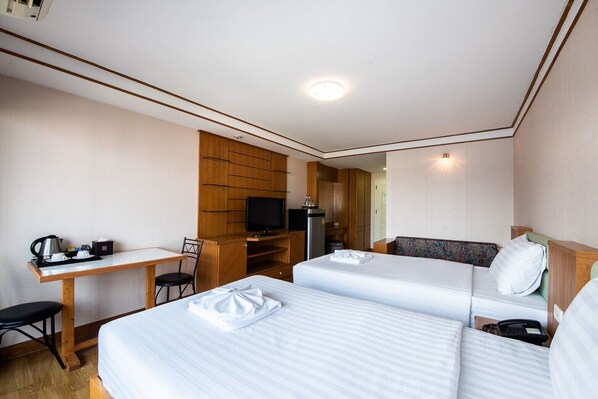 A hotel room with two beds, a desk, a television, and a kitchenette. - Roseate Ratchada (Bangkok)