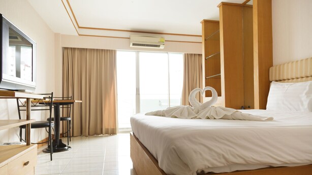 A hotel room with a bed, a desk with a chair, a television, and a large window with curtains.