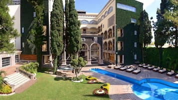 A hotel courtyard with a swimming pool, lounge chairs, and a fountain.
