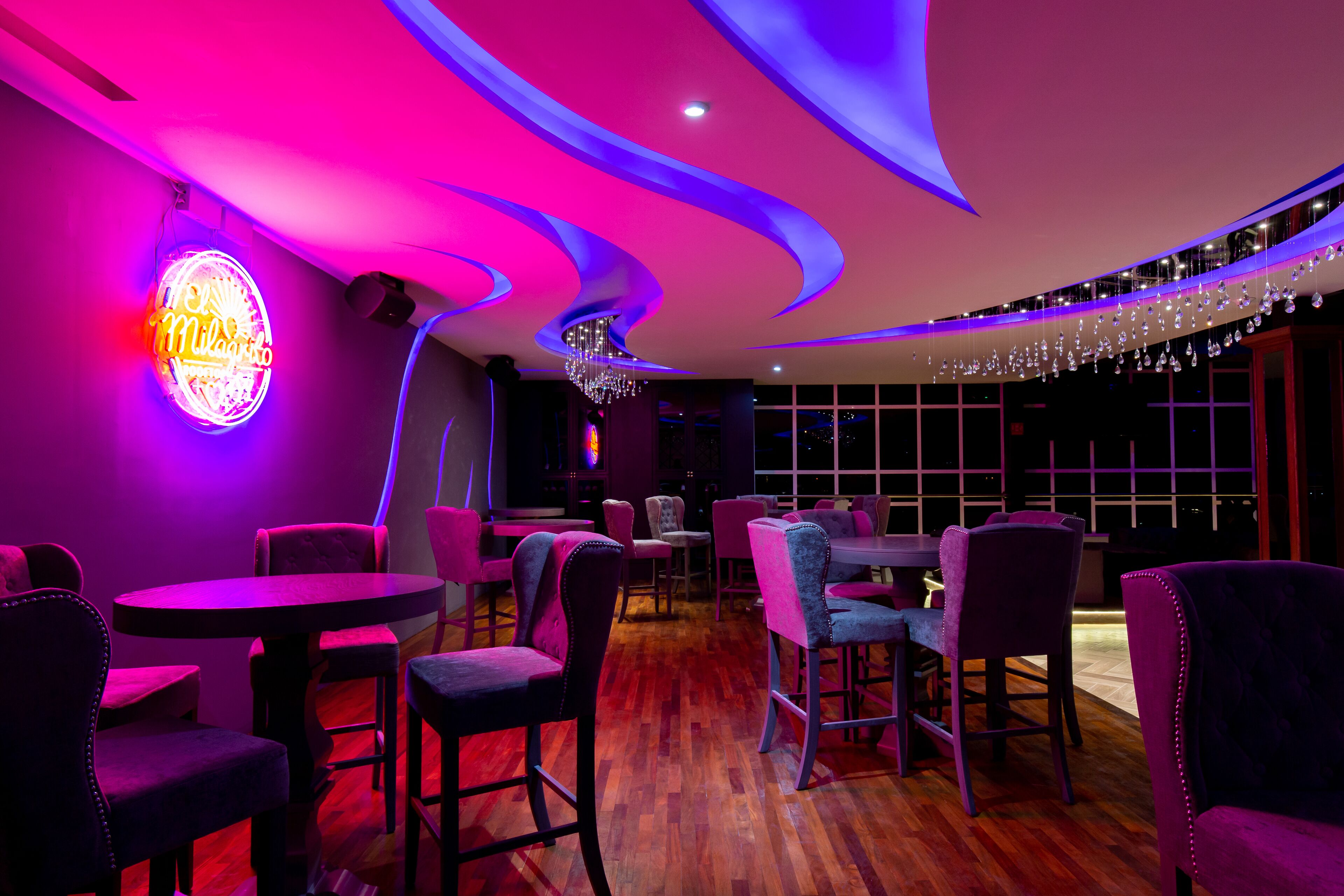 A restaurant with purple lighting, round tables, and velvet chairs.