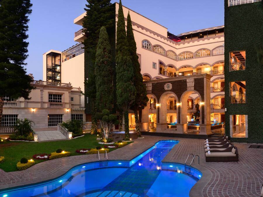 A luxurious hotel with a swimming pool, outdoor seating, and a well-maintained garden.