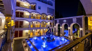 Un hotel de varios pisos con balcones, una fuente central y una zona de piscina.