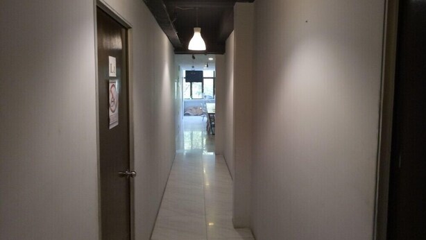 A narrow hallway with a door on the left, a sign on the wall, and a ceiling light. - Serenity Hostels (Kuala Lumpur)