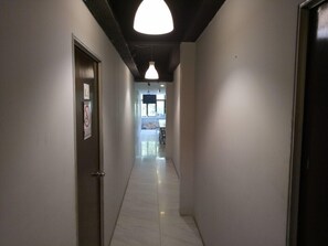 A narrow hallway with a door on the left, a sign on the wall, and a ceiling light. - Serenity Hostels (Kuala Lumpur)