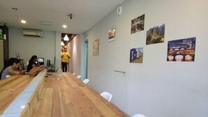 A long wooden table with white chairs in a room with light blue walls, air conditioning units, and various pictures on the walls. - Serenity Hostels (Kuala Lumpur)