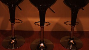 Three black bar stools with metal bases and a wall with three framed coffee cup artworks. - Serenity Hostels (Kuala Lumpur)