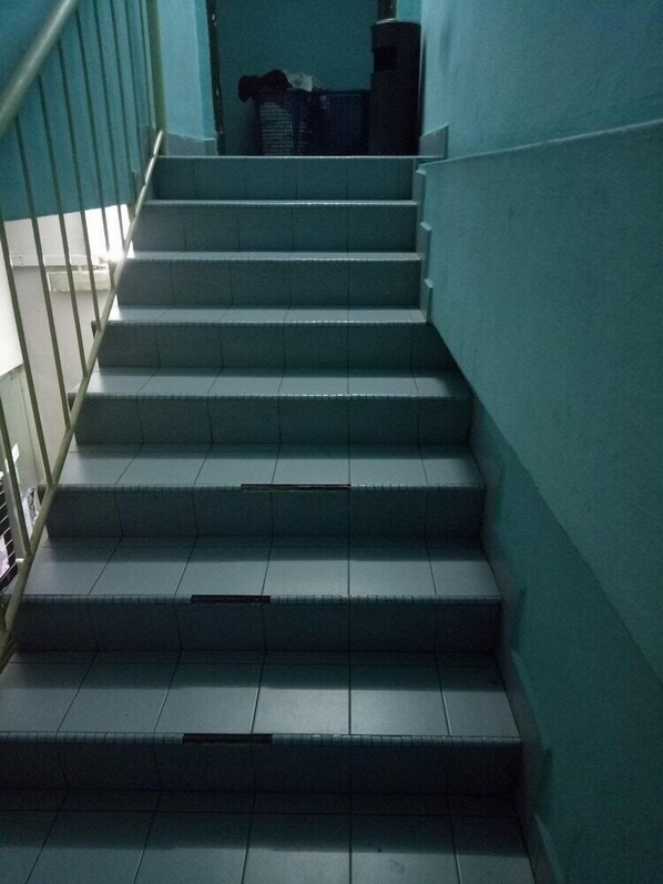 A set of stairs with a handrail on the left, leading to a landing area with a basket and a small table. - Serenity Hostels (Kuala Lumpur)