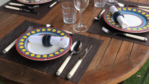 Une table ronde en bois, dressée pour le repas, avec des assiettes colorées, des couverts et des verres à vin.