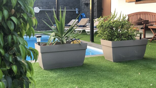 Un espace piscine agrémenté de gazon synthétique, de chaises longues et de plantes en pot.