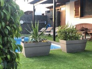 Ein Poolbereich mit Kunstgras, Liegestühlen und Kübelpflanzen.