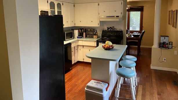 A kitchen with white cabinets, a black refrigerator, a microwave, a stove, and a sink. There is a fruit bowl on the counter and a trash can with a red lid. - Top floor suite (St. Albert)