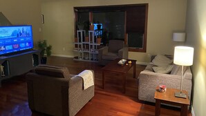 A living room with a flat-screen TV, two sofas, a coffee table, a lamp, and a window with blinds. - Top floor suite (St. Albert)