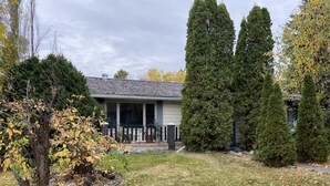 A residential house with a covered porch, a fenced yard, and several trees. - Top floor suite (St. Albert)