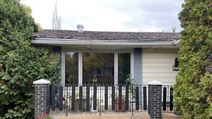 A residential house with a brick exterior, large sliding glass doors, a small porch, and a stone wall with a planter. - Top floor suite (St. Albert)