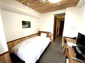 Habitació d'hotel amb sostre de fusta, un llit, escriptori amb ordinador i televisió.