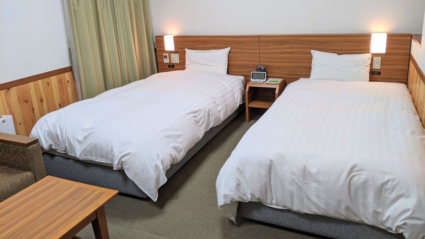 A hotel room with two single beds, bedside tables, a small desk, and a couch.