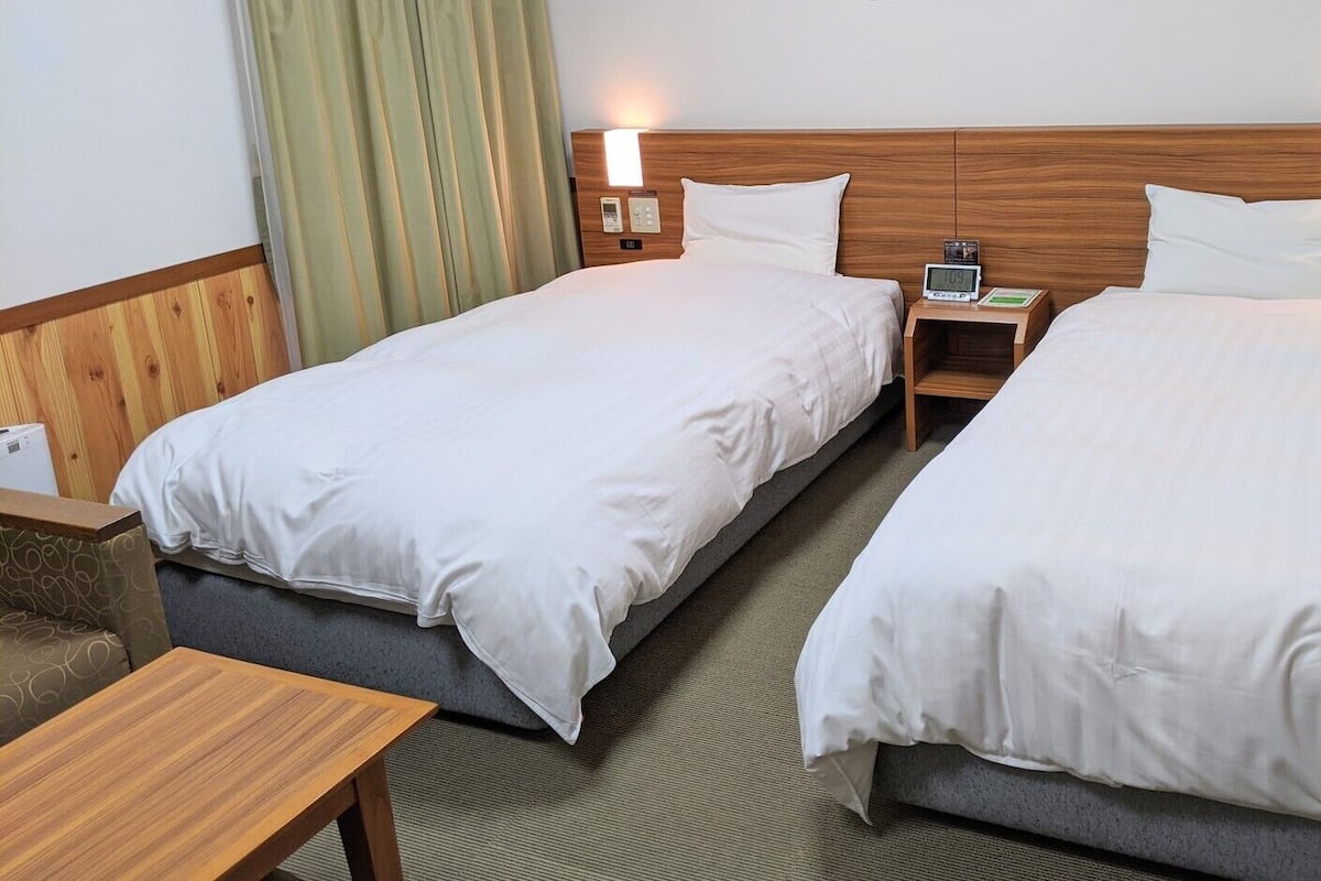 Une chambre d’hôtel avec deux lits simples, des tables de chevet, un petit bureau et un canapé.