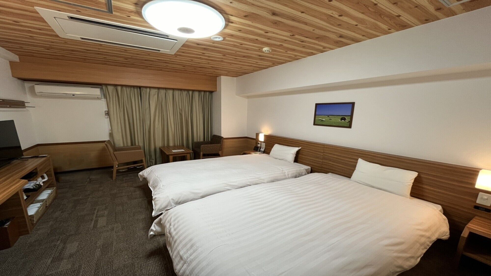 A hotel room with two beds, a desk, a chair, a TV, and an air conditioning unit.