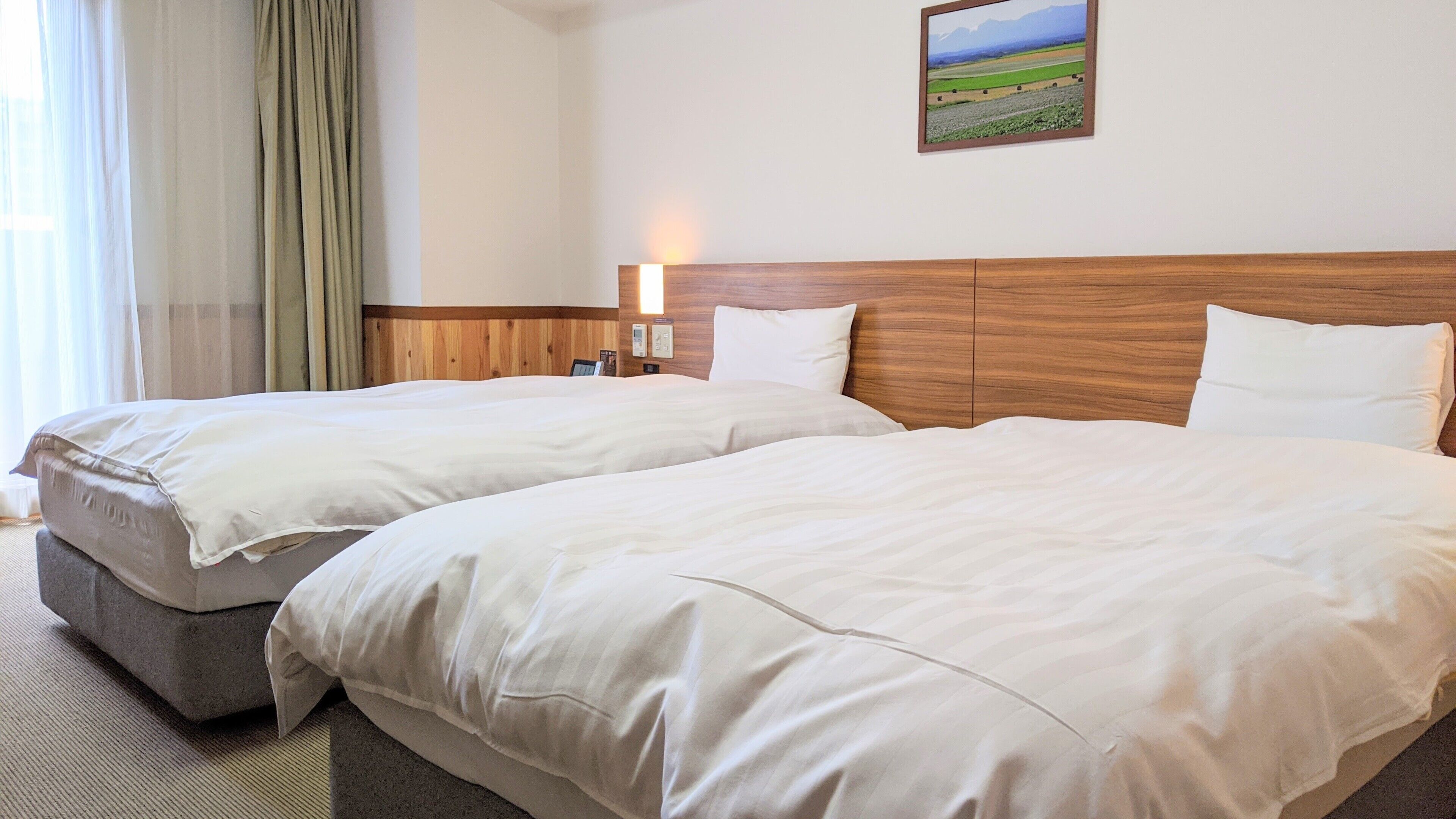 A hotel room with two beds, a wooden headboard, a nightstand, a lamp, and a painting on the wall.
