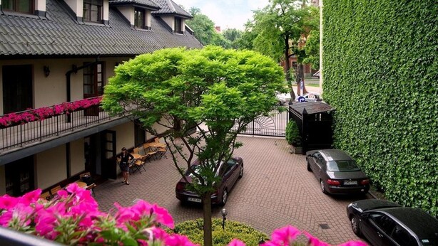A courtyard with a tree, parked cars, and a building with a tiled roof. - No.23 Premium Aparthotel (Kraków)