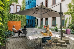 An outdoor seating area with tables and chairs, surrounded by greenery and a building with blue and white walls. - No.23 Premium Aparthotel (Kraków)