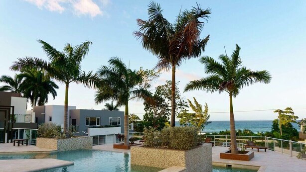Área de piscina com palmeiras, um edifício moderno e vista para o oceano.