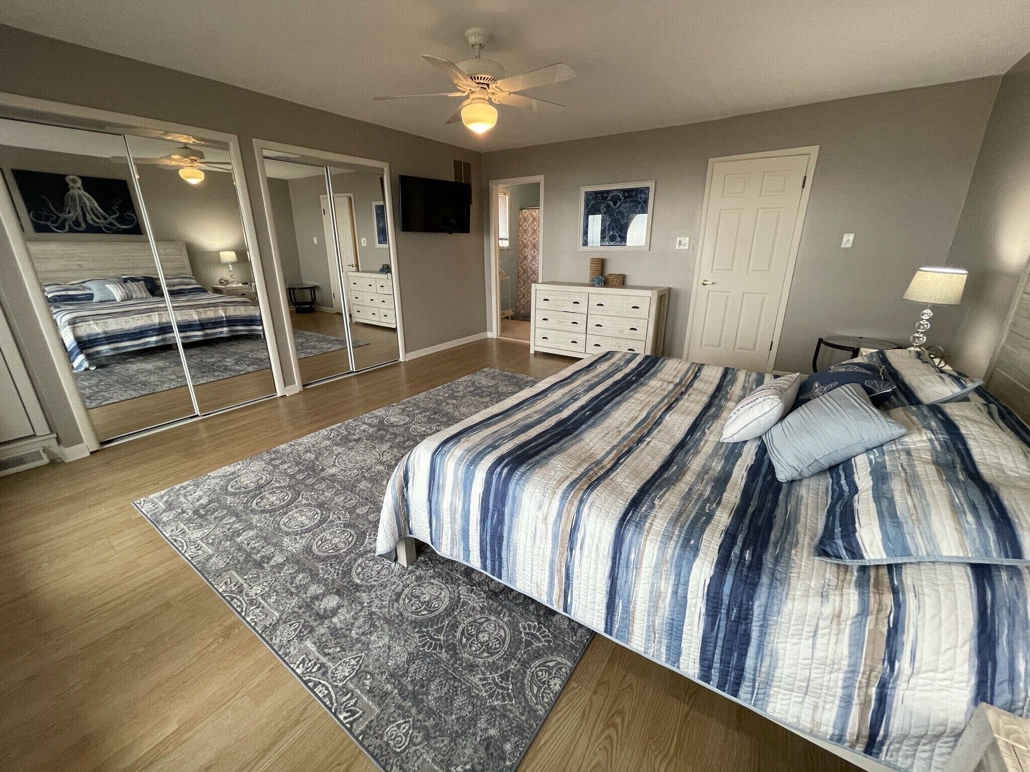 A bedroom with a large bed, a ceiling fan, a dresser, a TV, and a mirror.