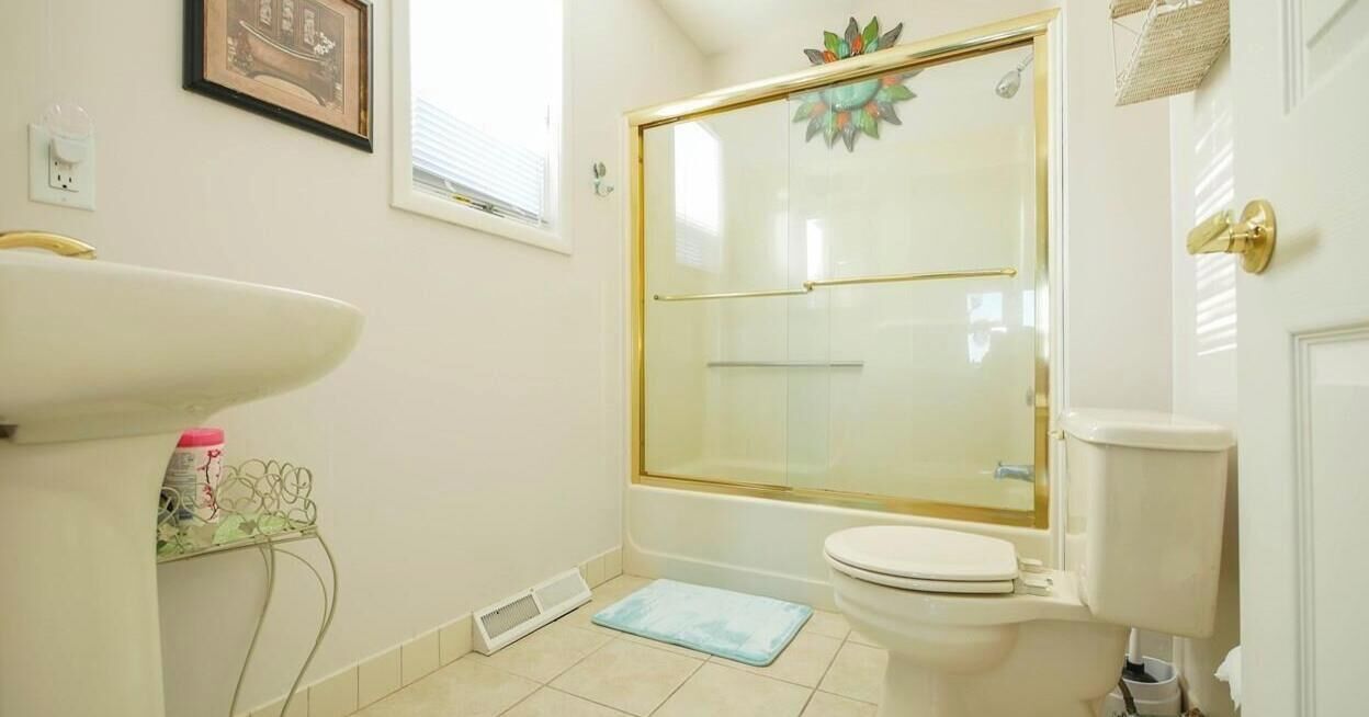 A bathroom with a white sink, a toilet, a shower with a glass door, and a small rug on the floor.