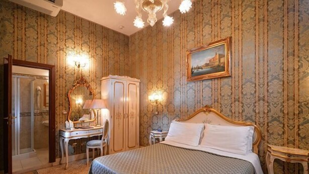 Een hotelkamer met een groot bed, een bureau met lamp, een kledingkast en een schilderij aan de muur.