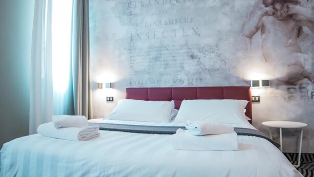 A hotel room with a large bed, white linens, a red headboard, and a wall mural. - Hotel Cannaregio 2357 (Venice)