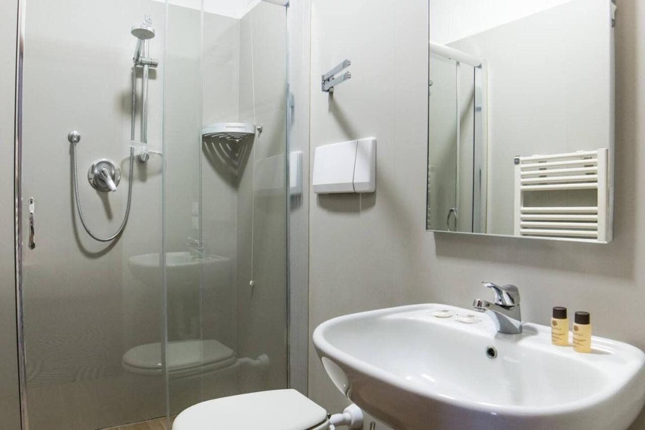 A modern bathroom with a glass-enclosed shower, a white sink with toiletries, and a mirror above the sink.
