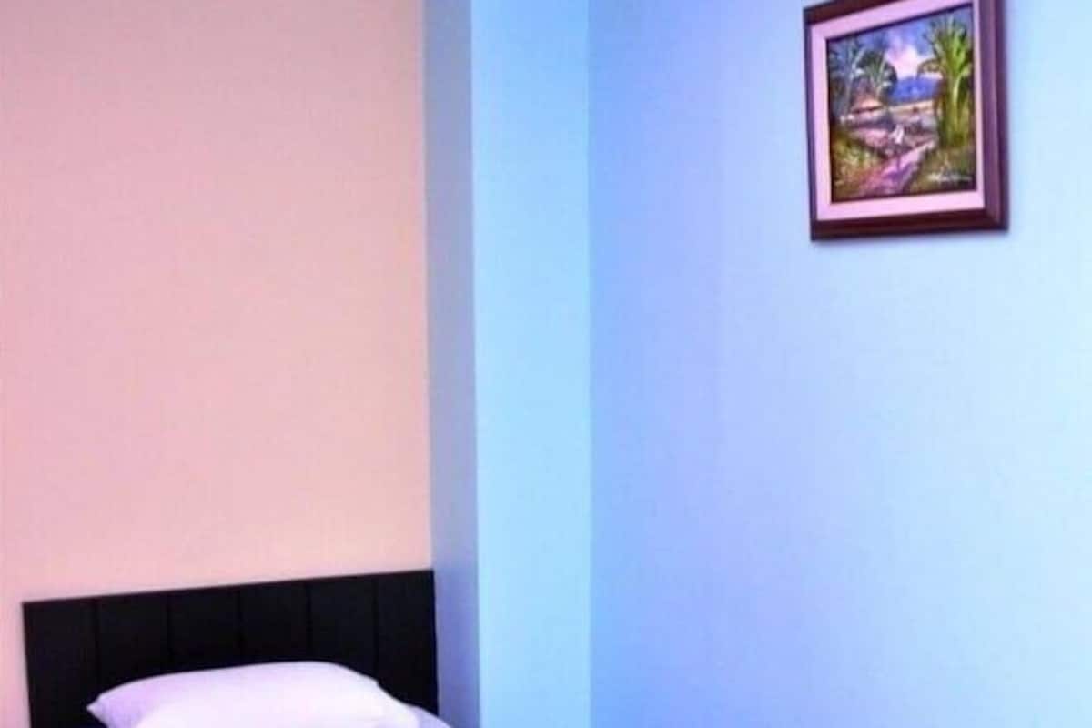 A single bed with a black headboard and a purple bedspread in a room with light blue walls and a framed picture on the wall.