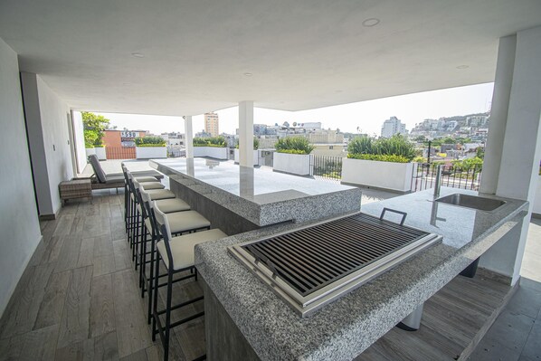 A modern outdoor kitchen area with a granite countertop, bar stools, and a built-in grill.