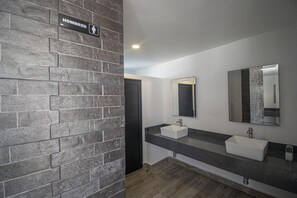 Un bagno moderno con parete in mattoni, due lavandini e uno specchio.