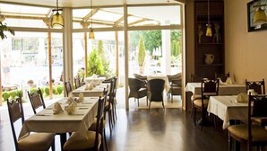 A restaurant with multiple tables and chairs, large windows, and hanging light fixtures. - Grand Hotel Nirvana (Nessebar)