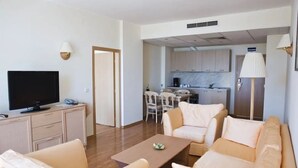 A modern living room with a flat-screen TV, beige sofas, a coffee table, and a kitchen in the background. - Grand Hotel Nirvana (Nessebar)