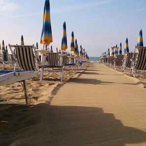 A beach with rows of striped beach chairs and umbrellas. - Hotel Madera (Jesolo)
