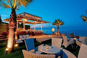 An outdoor seating area with wicker furniture and a covered bar, overlooking a body of water. - Maistros Exclusive Suites (Rethymno)