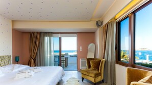 A hotel room with a bed, a chair, a view of the sea, and a balcony. - Maistros Exclusive Suites (Rethymno)